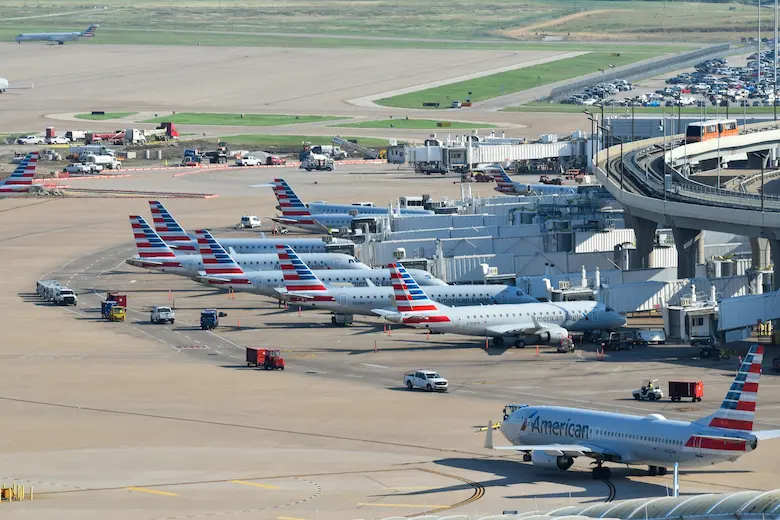 American Airlines planes lined up at gates at Dallas–Fort Worth International Airport with ground crews and vehicles operating on the tarmac.